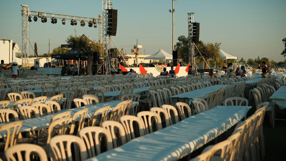 Escenario al aire libre con arreglos de bocinas en estructura de truss frente a mesas para invitados