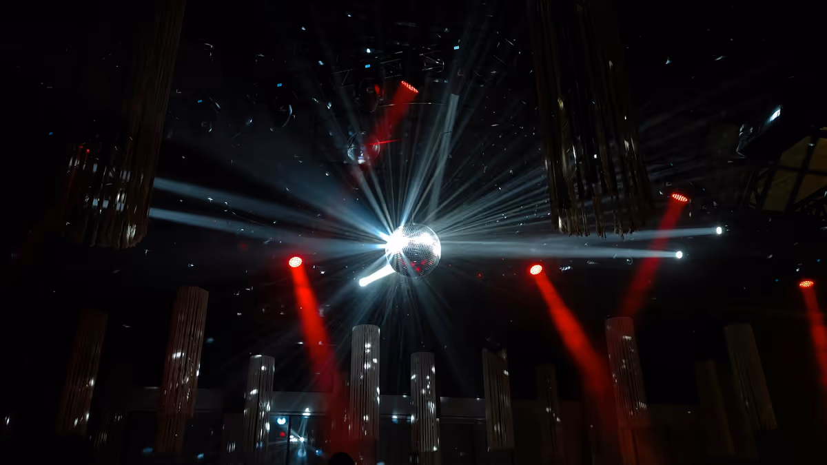 Bola disco iluminada con haces rojos y blancos en salón oscuro
