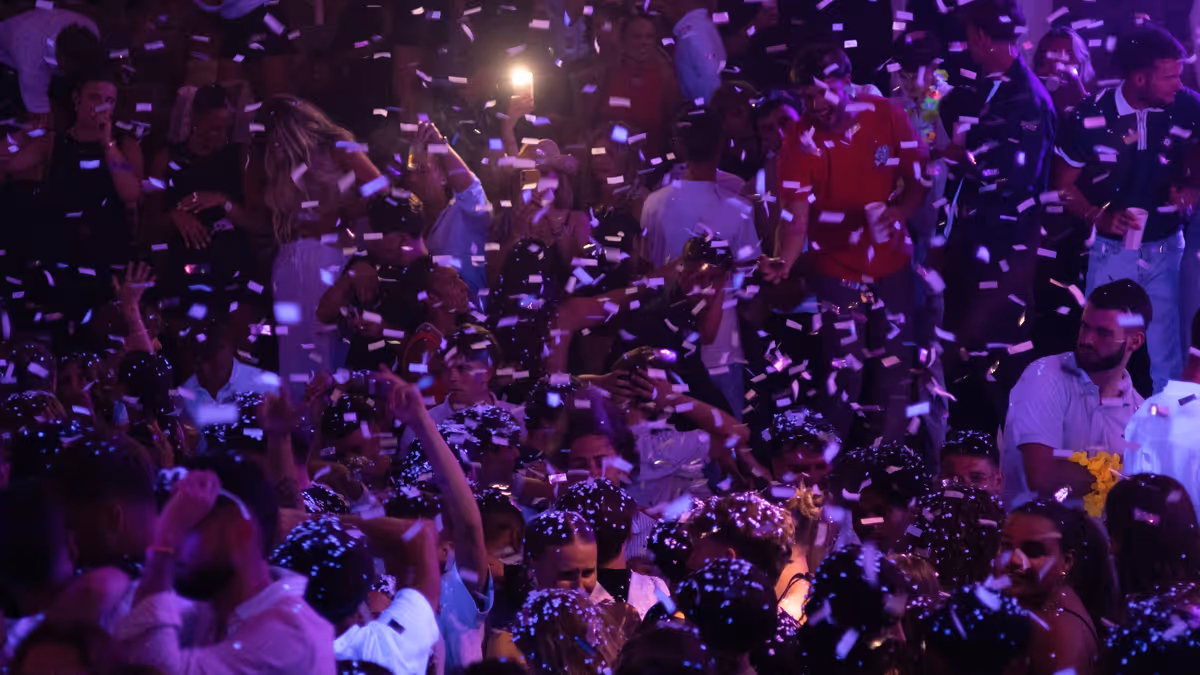 Personas bailan bajo confeti blanco con luces moradas