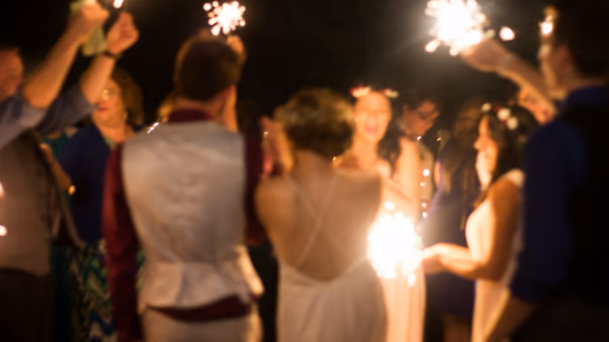 Invitados de boda de espaldas sosteniendo bengalas encendidas por la noche
