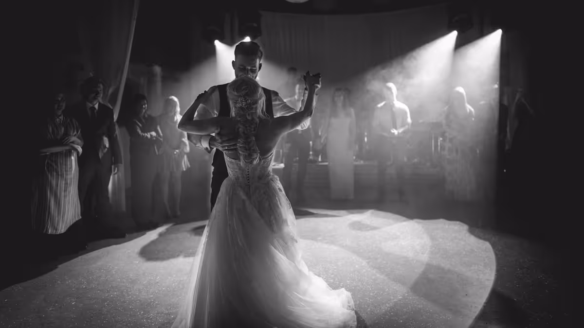 Pareja bailando bajo haces de luz con humo en una pista de boda, en blanco y negro
