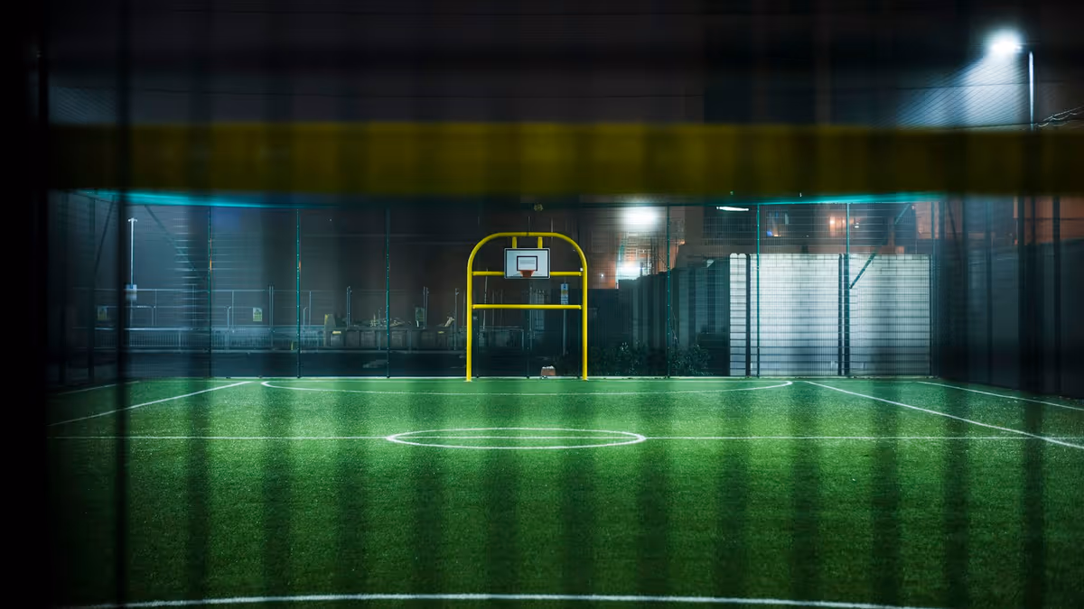 Cancha deportiva iluminada por reflectores perimetrales durante la noche