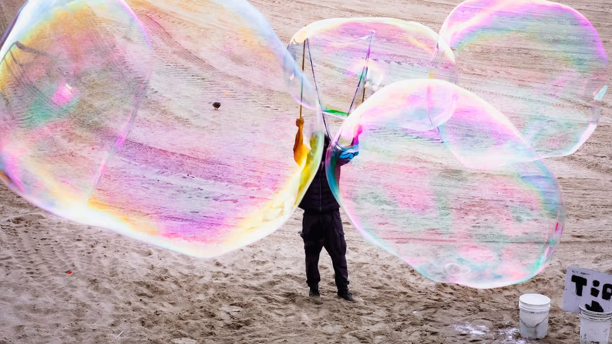 Persona creando burbujas iridiscentes gigantes sobre arena junto al mar