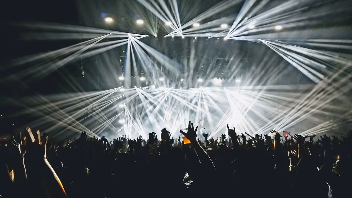 Personas bailando en interior con luces beam visibles entre la neblina
