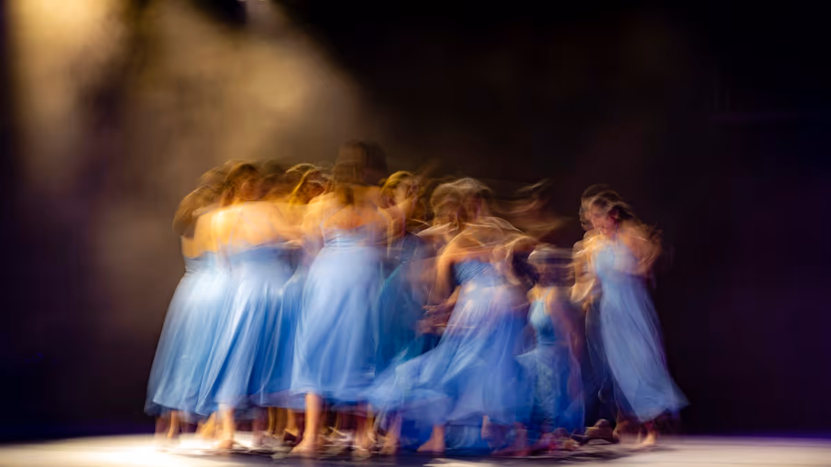 Grupo de mujeres con vestidos blancos bailando bajo iluminación wash