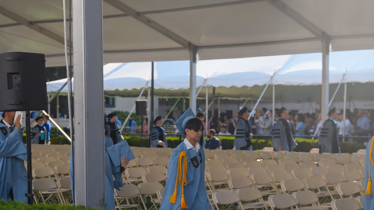 Graduados con túnicas azul claro caminan junto a filas de sillas