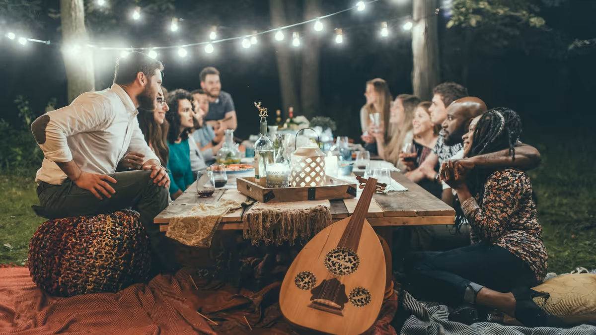 Personas cenando al aire libre sobre mantas en un jardín nocturno