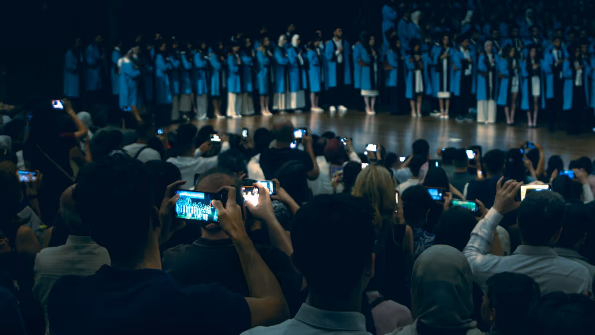 Público graba graduados con togas azules en escenario iluminado