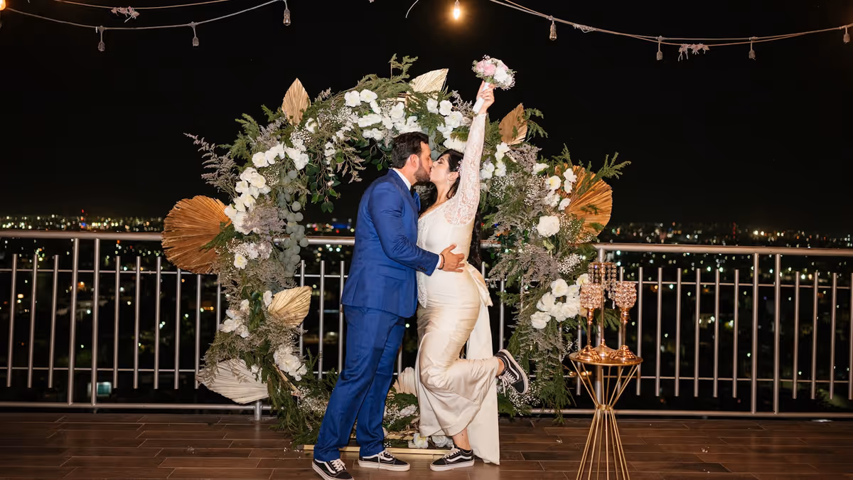 Novia y novio se besan bajo arco floral nocturno