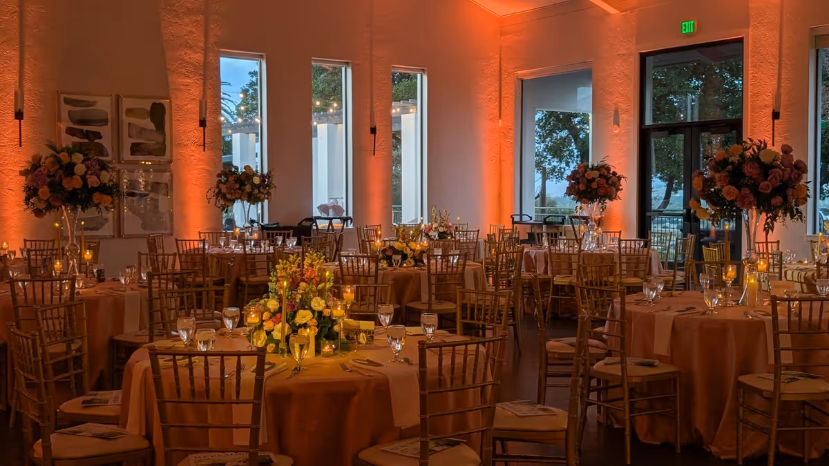 Sala elegante con mesas florales y luz naranja para cena de boda