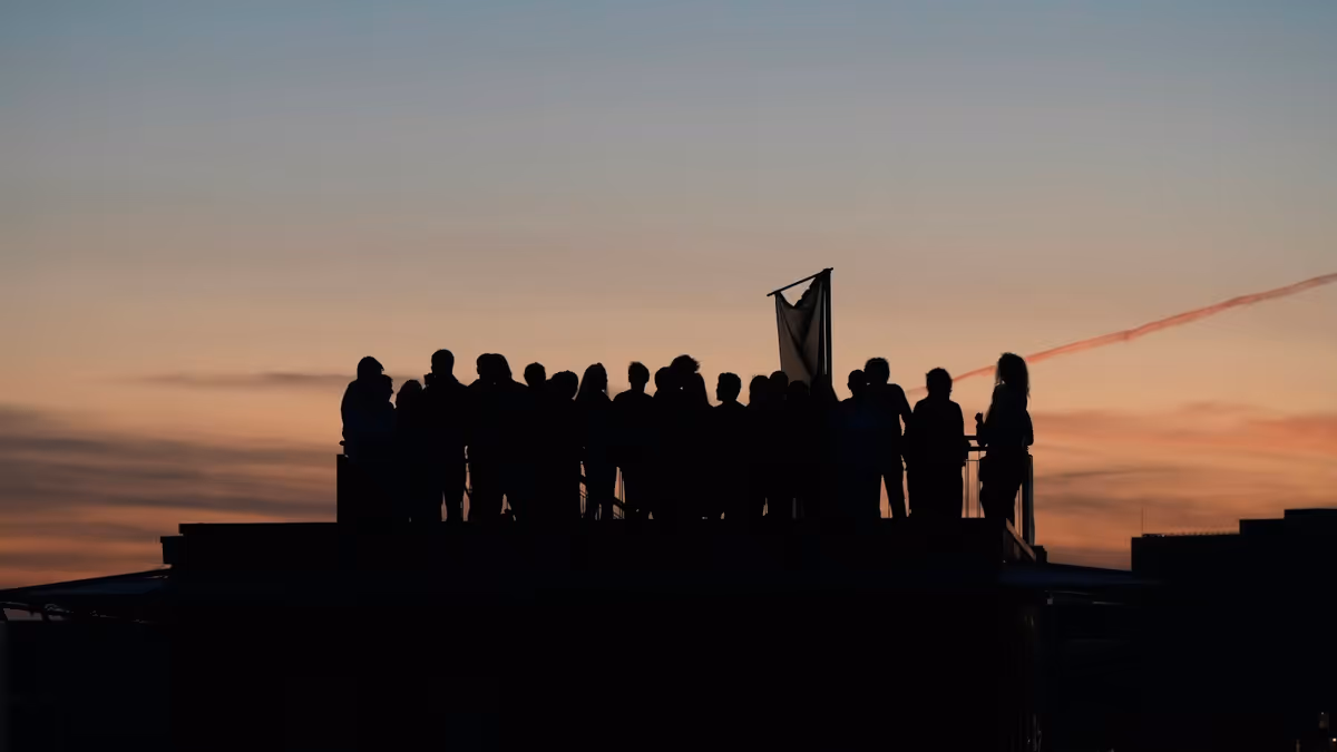 Siluetas de asistentes en azotea bajo cielo colorido al atardecer