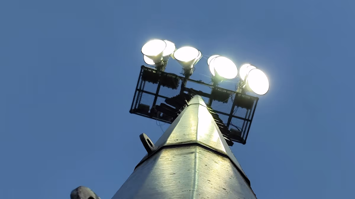 Torre de iluminación con cabezal de lámparas encendidas contra el cielo