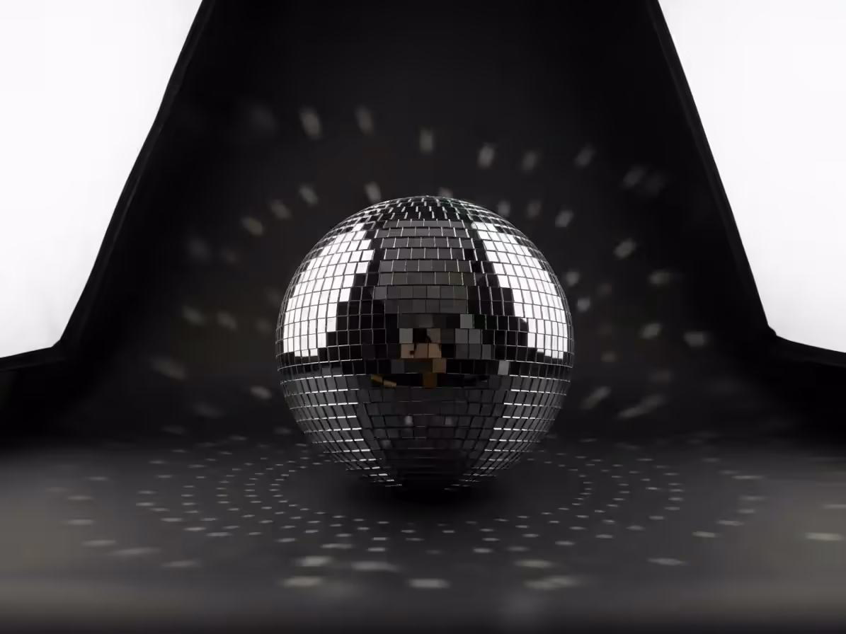 Bola de espejos plateada sobre un piso oscuro que proyecta puntos de luz en el fondo curvo de un estudio