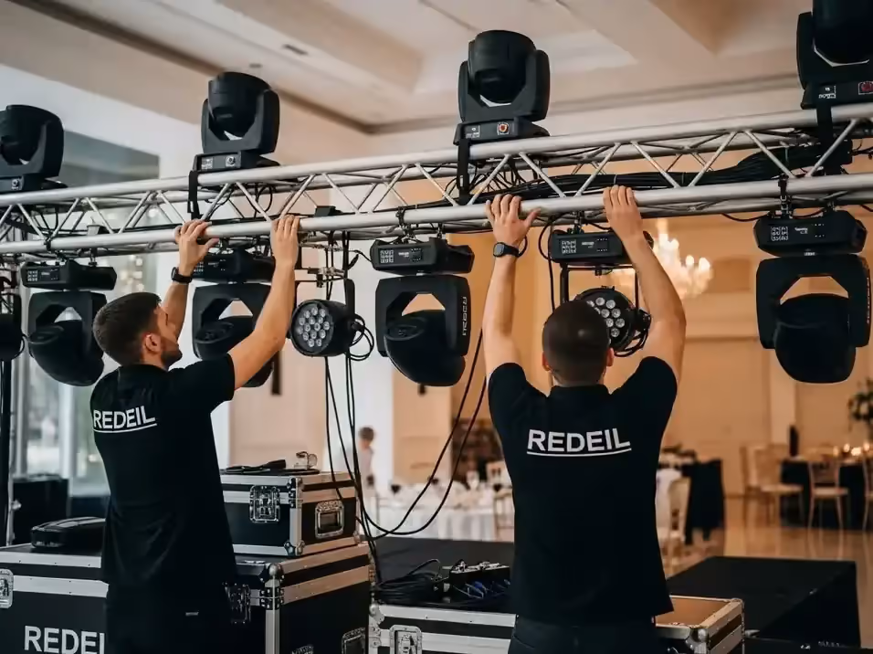 Dos técnicos colocando cabezas móviles en un truss de aluminio dentro de un salón
