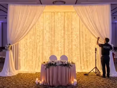Mesa de novios ancha con invitados a los costados frente a un fondo de luz continuo