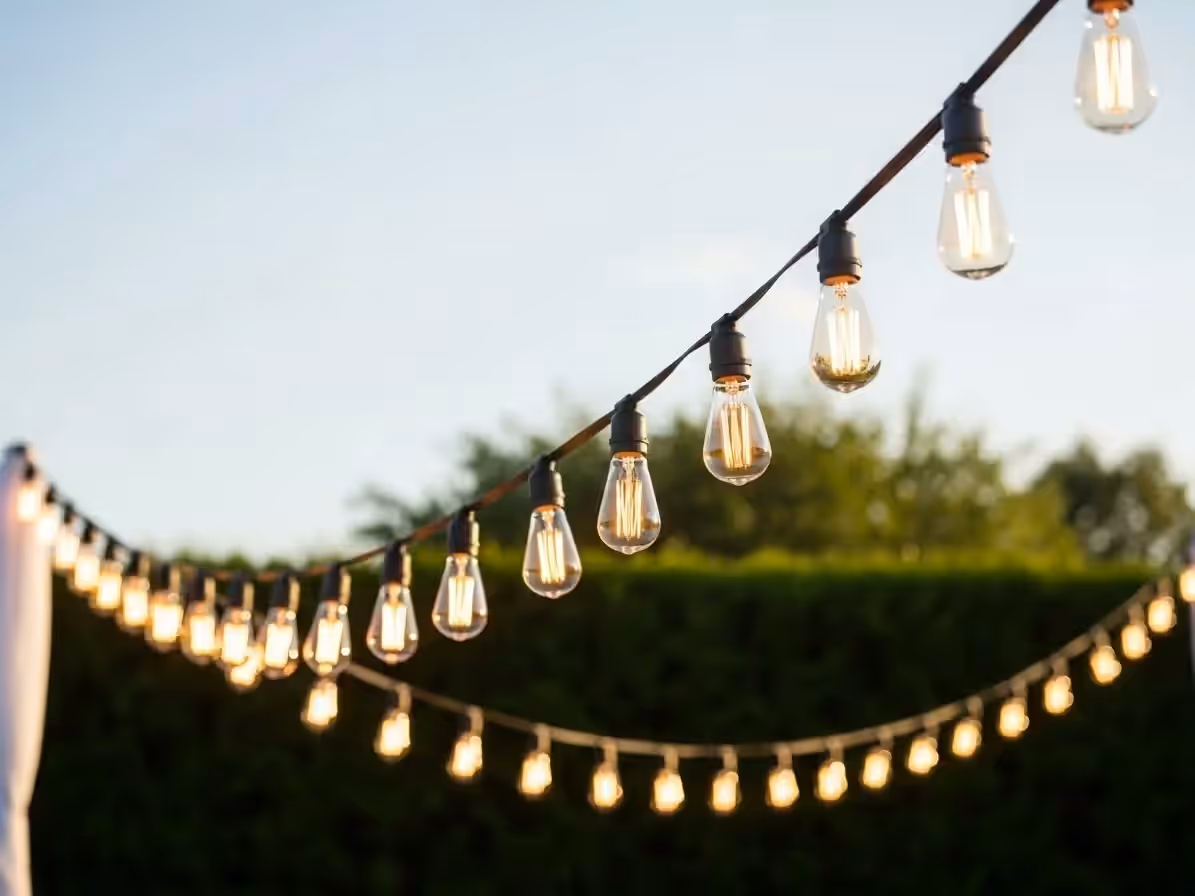 Cielo de guirnaldas vintage sobre recepción de boda en jardín al atardecer