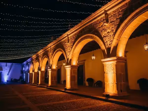 Corredor de arcos coloniales encendido de noche junto a luces de cadena