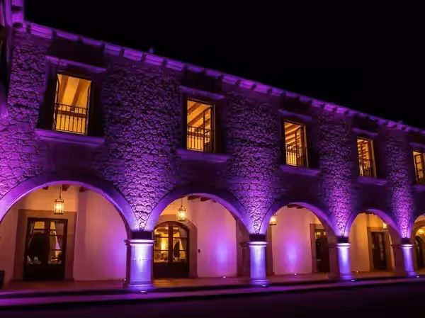 Portada de arcos coloniales encendida en violeta al anochecer