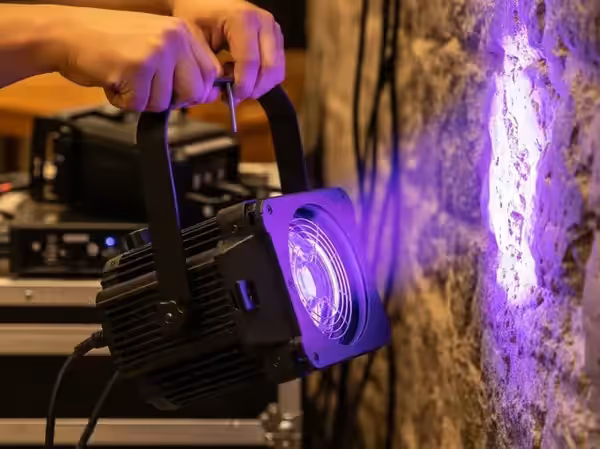 Ajuste técnico de un uplighter en morado frente a una fachada antes del evento