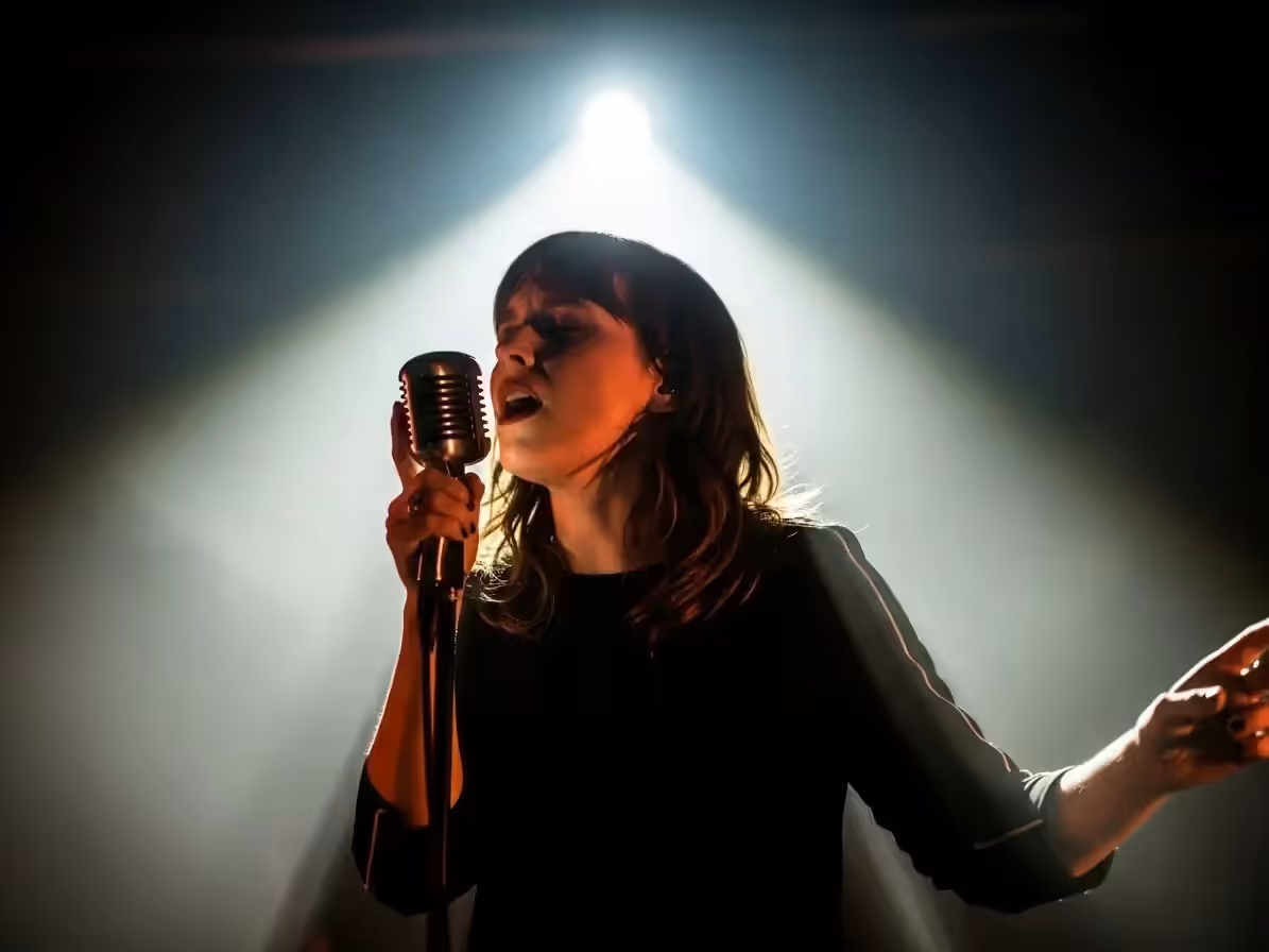 Vocalista al micrófono recortado por el haz de un follow spot en concierto