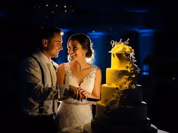 Corte de pastel con el círculo de luz reducido sobre las manos de los novios