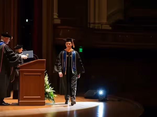 Estudiante con toga cruzando el escenario bajo el círculo del seguidor