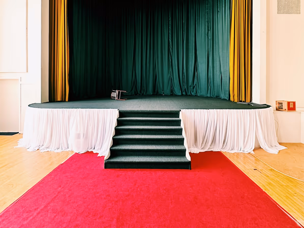 Escenario con alfombra roja, cortinas verdes y escalones centrales