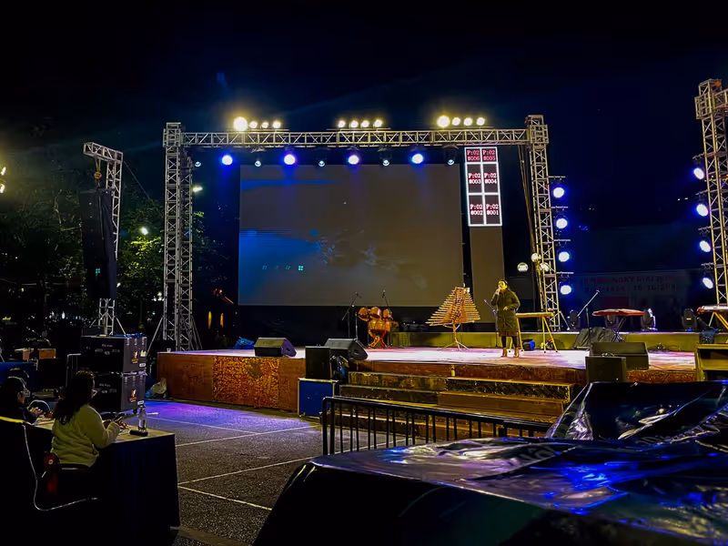 Escenario exterior con pantalla y asistentes durante la noche